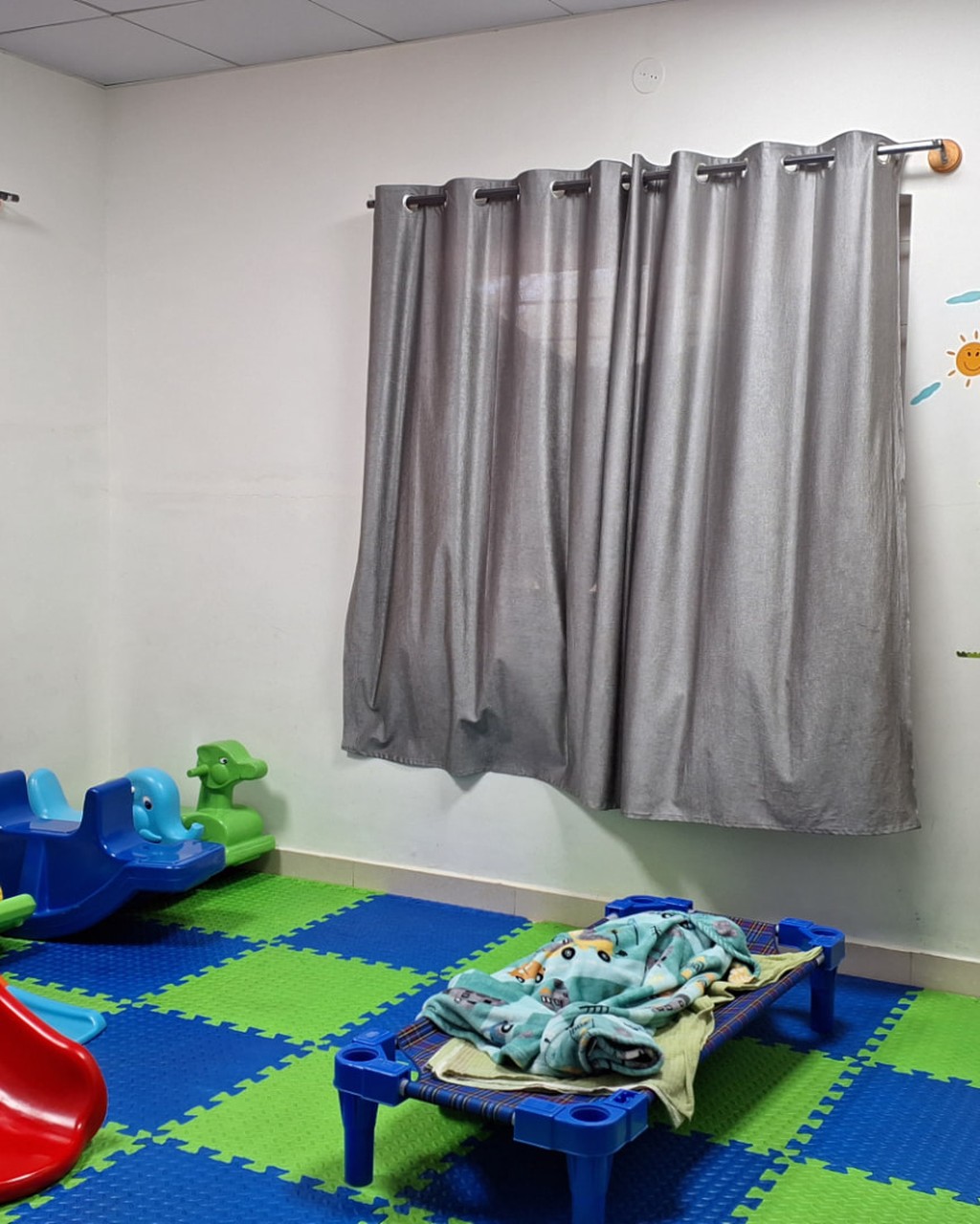 A bright daycare playroom with a red slide, rocking toys, soft mats and rest areas for children