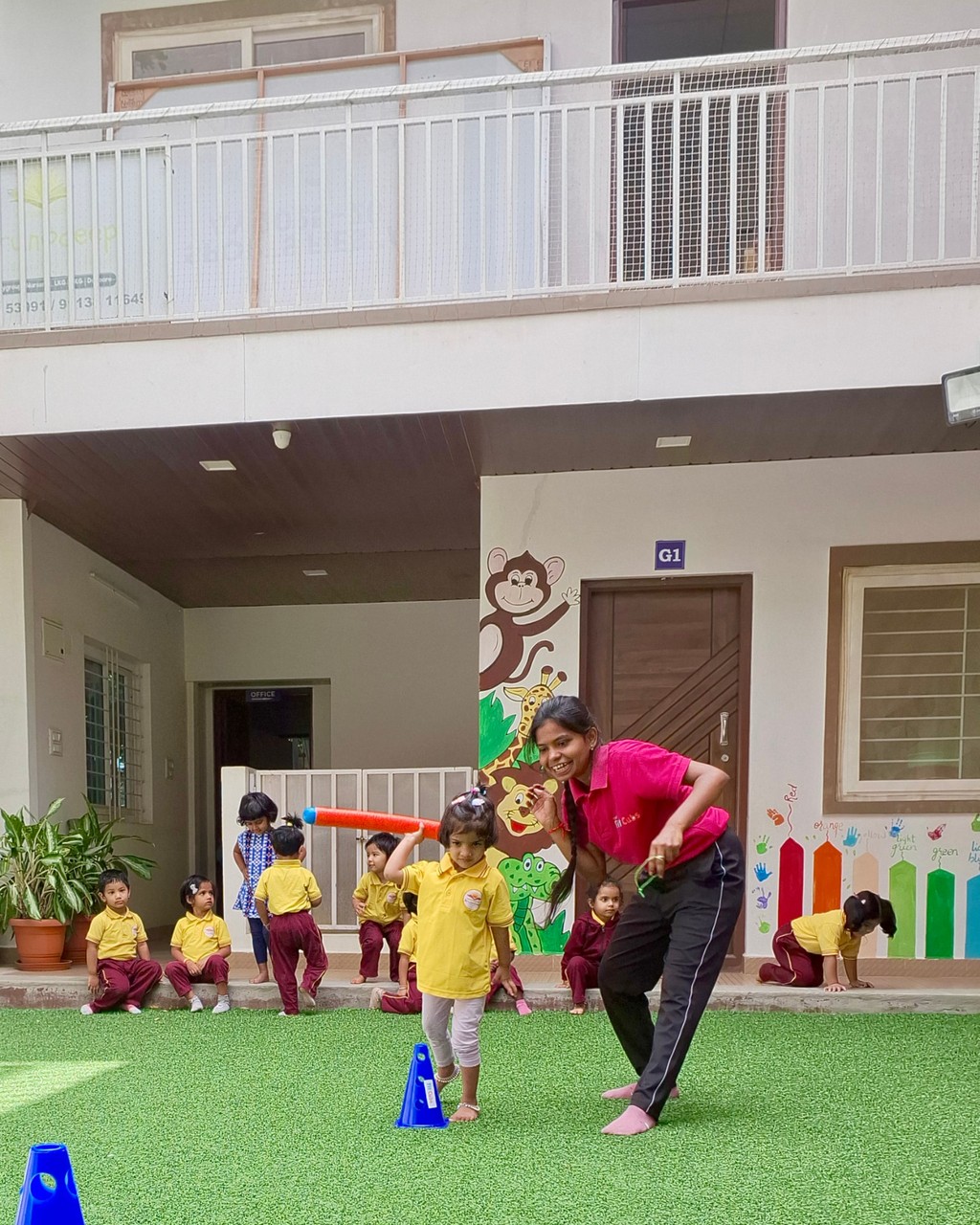 A teacher playing outdoors with children on a bright green lawn, using colourful sports equipment and games