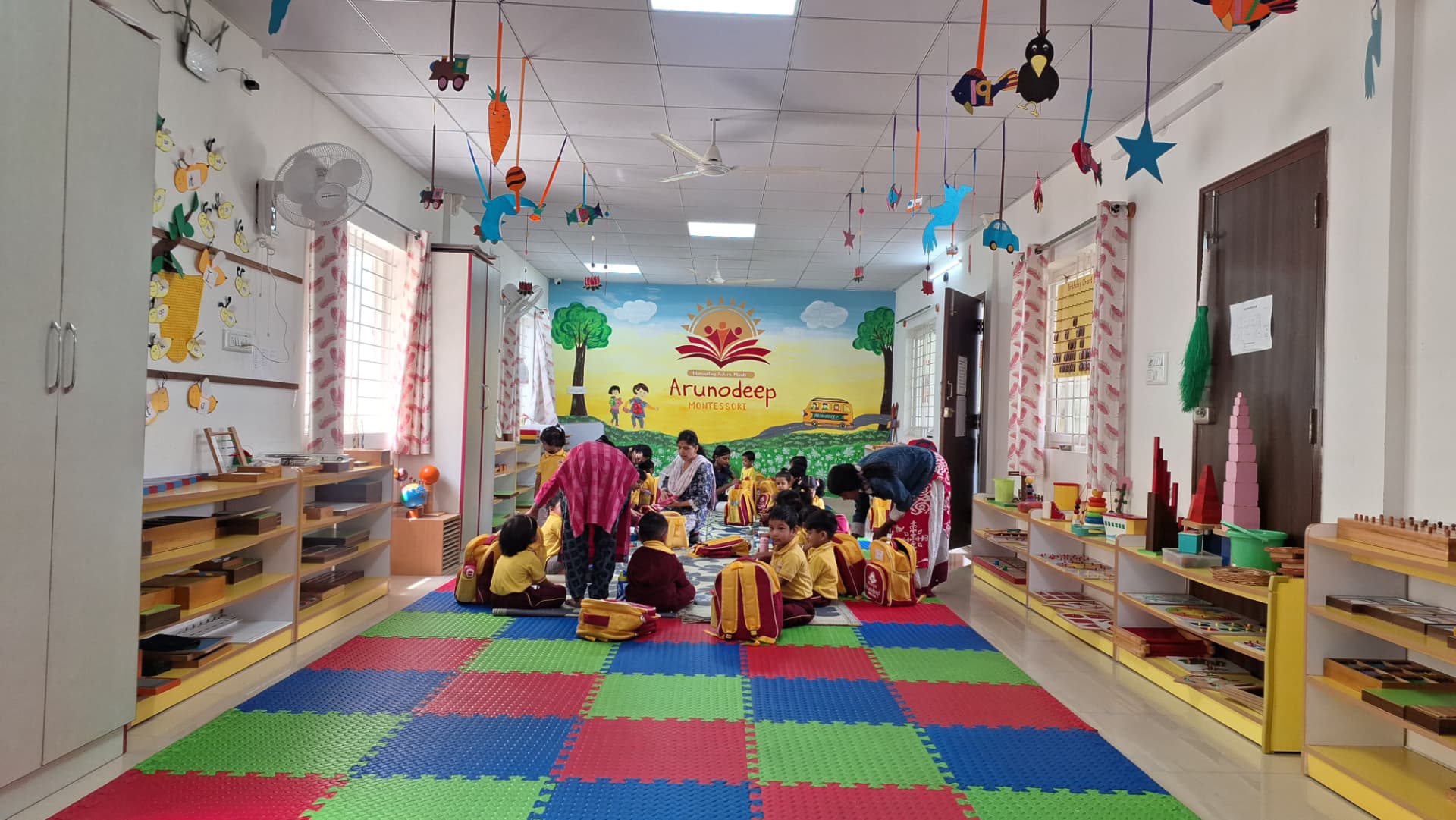 Children working with Montessori materials on the floor of the bright Arunodeep classroom