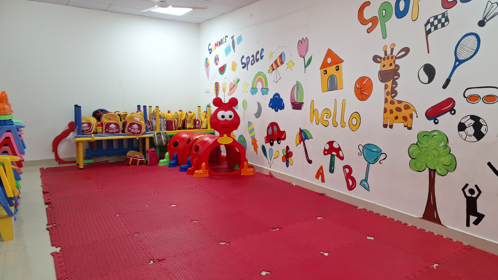 Colourful indoor play room with soft mats, play tunnel and hand-painted wall murals